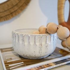 a white bowl sitting on top of a wooden table next to a book and vase