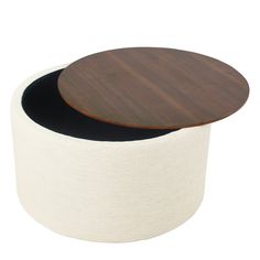 a round wooden table sitting on top of a white fabric covered ottoman with a black bottom