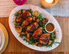 a white plate topped with chicken and greens next to a cup of sauce on a wooden table