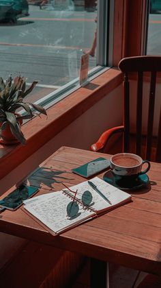 a wooden table topped with a cup of coffee next to a window