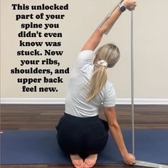 a woman sitting on the floor with her legs up and holding a pole above her head