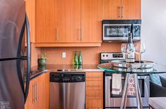 a small kitchen with stainless steel appliances and wood cabinets, along with a glass top table