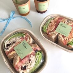 two plastic containers filled with sandwiches next to bottles of wine and a blue ribbon on the table