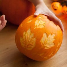 a child's hand is holding an orange ball with leaves painted on it and pumpkins in the background