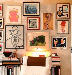 a living room filled with lots of framed pictures on the wall above a white chair