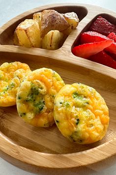 three small muffins on a wooden plate with strawberries and other food items