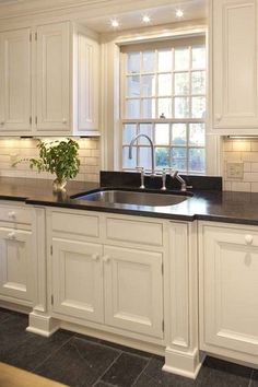 a kitchen with white cabinets and black counter tops is pictured in this image, there are lights on the windows above the sink