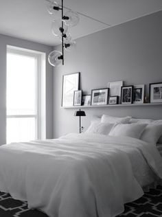 a white bed sitting in a bedroom next to a window with pictures on the wall