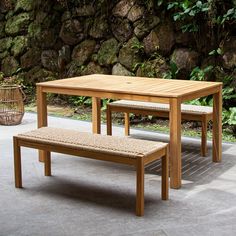 a wooden table with two benches next to a stone wall and green plants in the background