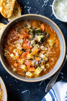 a bowl of pasta soup with bread on the side