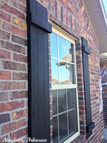 a brick building with black shutters on the windows and side of it is shown