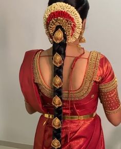 a woman wearing a red and gold sari with braids in her hair, looking down