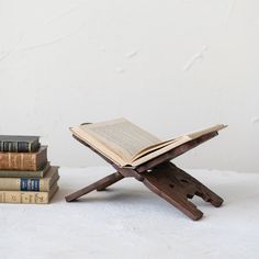 an open book sitting on top of a wooden stand next to three books in front of a white wall