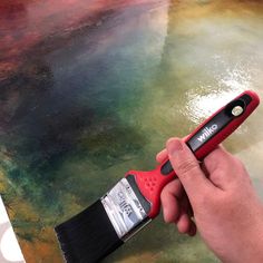 a hand holding a paint brush over a painting that has been dyed red and green