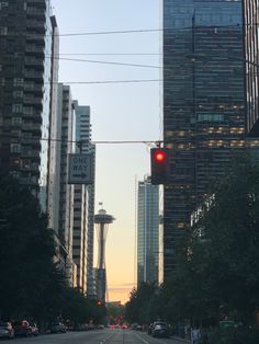 a red traffic light hanging over a street next to tall buildings in a city at sunset