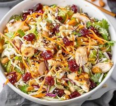 a salad with chicken, cranberries and shredded carrots in a white bowl