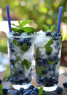 two glasses filled with blueberries and mint sprits next to each other on a table