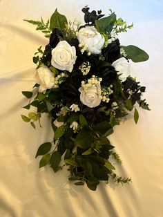 a bouquet of white roses and greenery on a bed