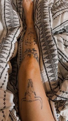 a person laying on top of a bed covered in blankets and pillows with tattoos on their legs