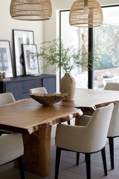 a dining room table with chairs and a vase on top of it in front of a large window