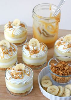 several desserts in small glass dishes on a wooden table with bananas and other toppings