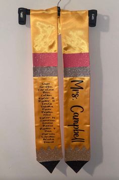 two yellow and pink ribbons with writing on them hanging from a hook against a white wall