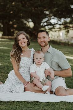 a man, woman and baby are sitting on a blanket in the grass smiling at the camera