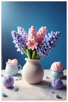 crochet flowers in a vase with balls of yarn around it on a table