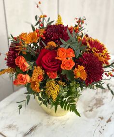 a vase filled with red, orange and yellow flowers on top of a white table