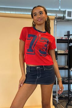 Also available in Olive and Black. Product Deets Red jersey mesh with navy number tee 100% polyester Navy trim detail Outlined 73 number graphic Full length baby tee fit Size small measures 17” long in front Runs true to size Model Info Kayleen is 5’6. Waist: 25" Bust: 32B Wearing size Small. Red Y2k Crew Neck T-shirt, Y2k Letter Print Top For College, Y2k Style Letter Print Top For College, Y2k Letter Print College Top, Y2k Red Graphic Print Top, Red Crew Neck Top For College, Red Sporty Tops For College, Sporty Red Tops For College, Trendy Red T-shirt For Sports