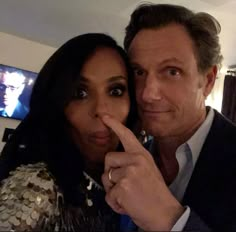 a man and woman are posing for a photo in front of a television screen with their finger up to the camera