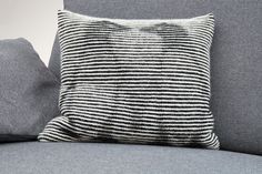 a black and white striped pillow sitting on top of a gray couch next to pillows