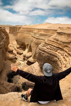 a man sitting on the edge of a cliff with his arms wide open in front of him