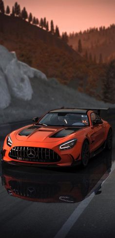 an orange sports car driving on a road near mountains and trees in the background at sunset