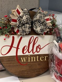 a wooden sign that says hello winter with bows on it and some candy in the background