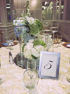 the table is set with flowers and wine glasses on it, along with a framed monogram