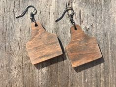 two wooden earrings hanging from hooks on a piece of weathered wood with black metal earwires