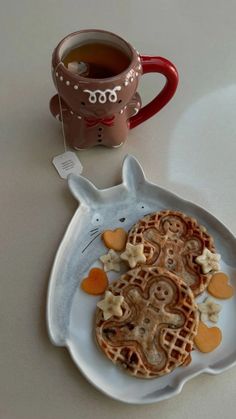 a white plate topped with waffles next to a cup of tea and a mug