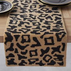 a leopard print table runner with black and gold plates on the side, next to it