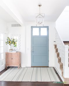 a blue door is in the middle of a white room with wood floors and stairs