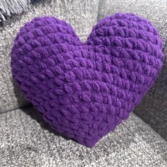 a purple crocheted heart sitting on top of a gray couch next to pillows