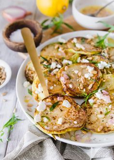 a white plate topped with potato cakes next to bowls of other food and utensils