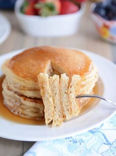 a stack of pancakes sitting on top of a white plate next to a bowl of fruit