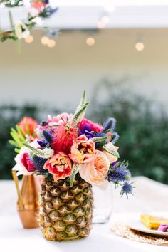 a pineapple vase filled with colorful flowers on top of a white table covered in lights