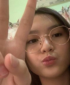 a woman wearing glasses making the v sign with her fingers