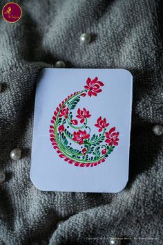 a white coaster with red flowers and green leaves on it sitting on a gray blanket