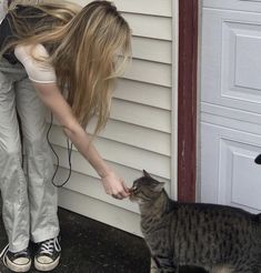 a woman is petting a cat on the side of a house while another looks at her