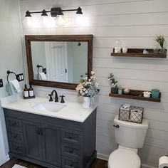 a white toilet sitting next to a sink in a bathroom under two wooden shelves filled with flowers