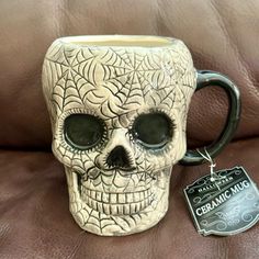 a ceramic skull mug sitting on top of a brown leather couch next to a tag