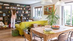 a woman standing in the middle of a living room next to a table with fruit on it